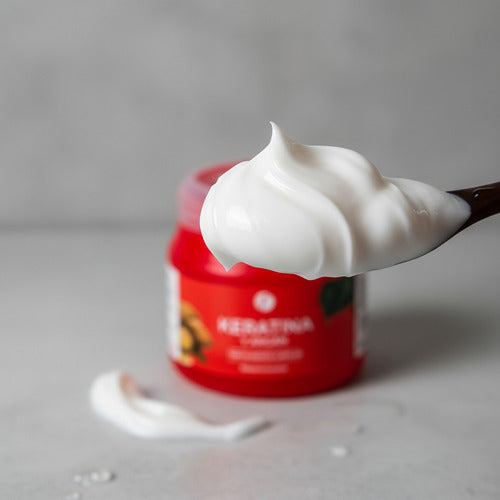 Baño de crema Distriwil con keratina y argán, textura cremosa blanca sobre una cuchara con envase rojo de fondo