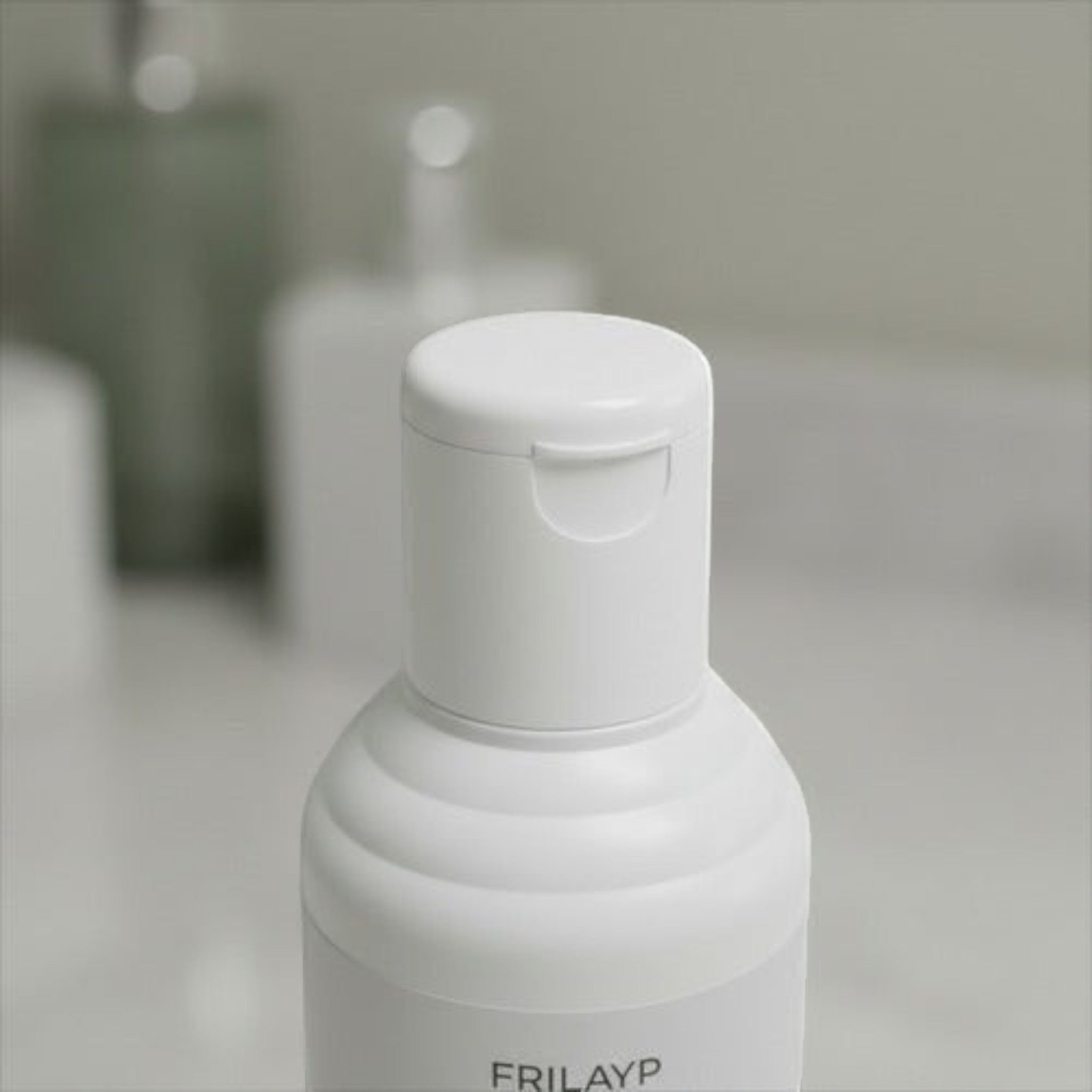 Botella de shampoo Frilayp Pistacho de Distriwil con tapa blanca abatible en un baño luminoso