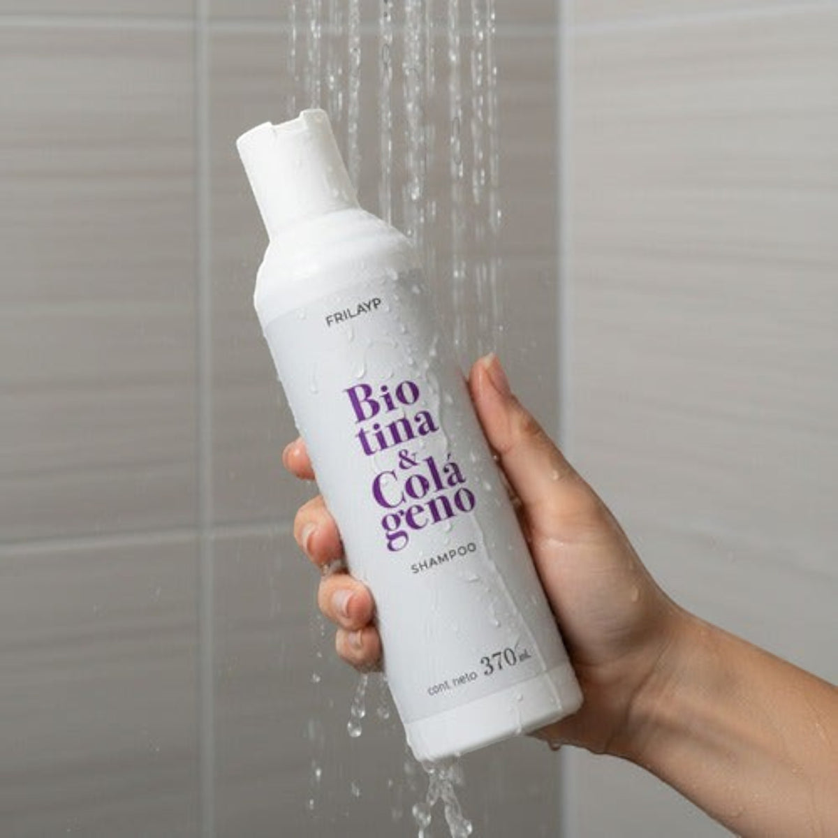 Mano sosteniendo botella de Shampoo Frilayp Biotina y Colágeno bajo la ducha para fortalecer el cabello