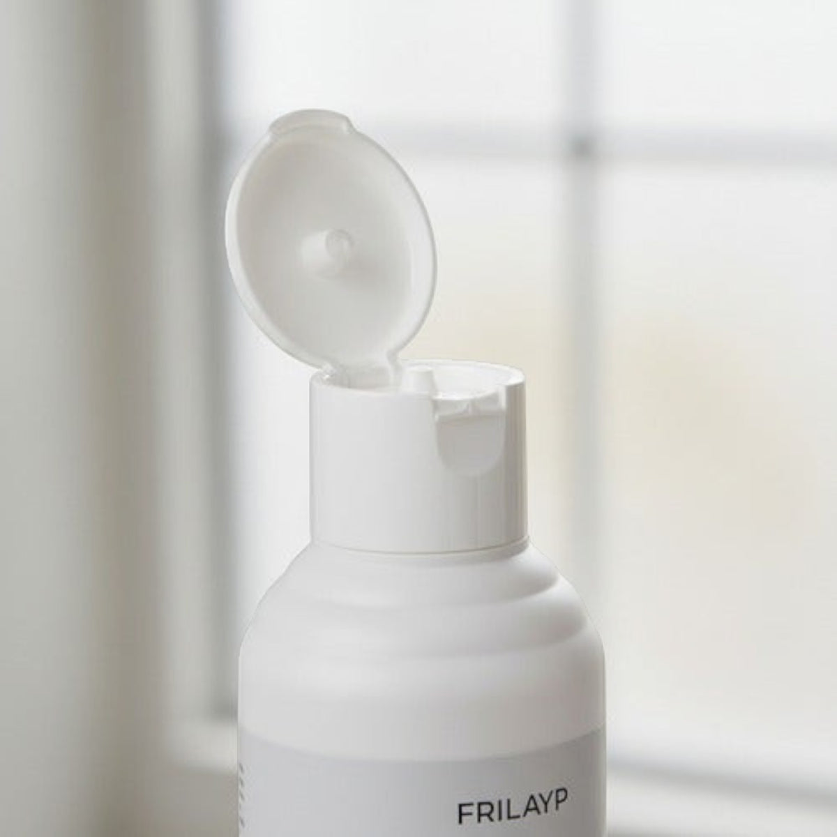 Envase de shampoo Distriwil Frilayp con tapa blanca abierta, diseñado para fortalecer el cabello con biotina.