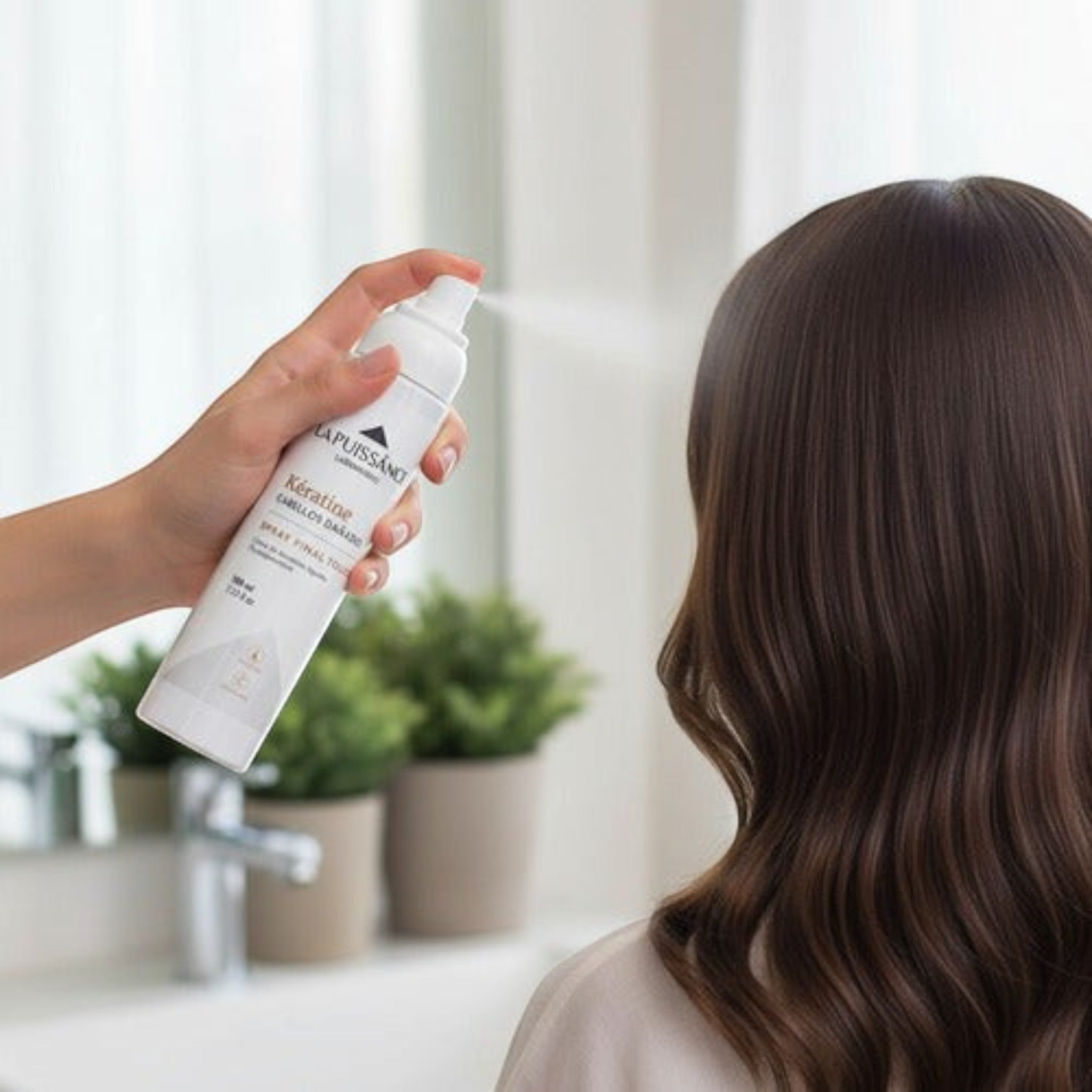 Mujer aplicando spray reparador de keratina Distriwil La Puissance sobre su cabello castaño para dar brillo y suavidad