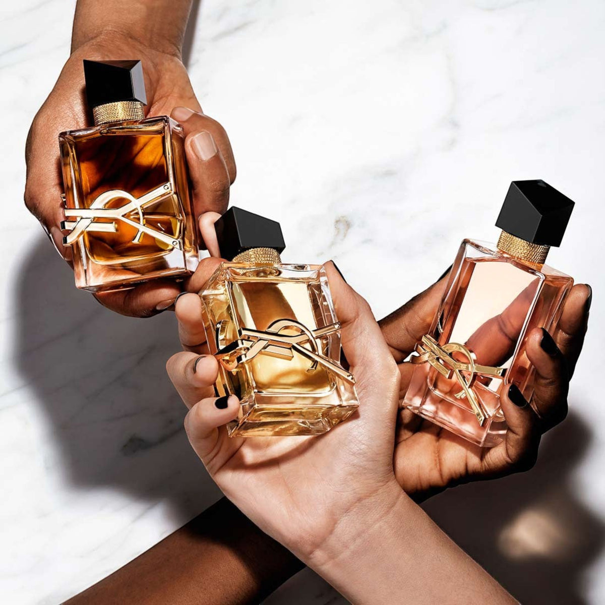 Tres frascos de perfume Yves Saint Laurent Libre sostenidos por manos sobre fondo de mármol de Distriwil